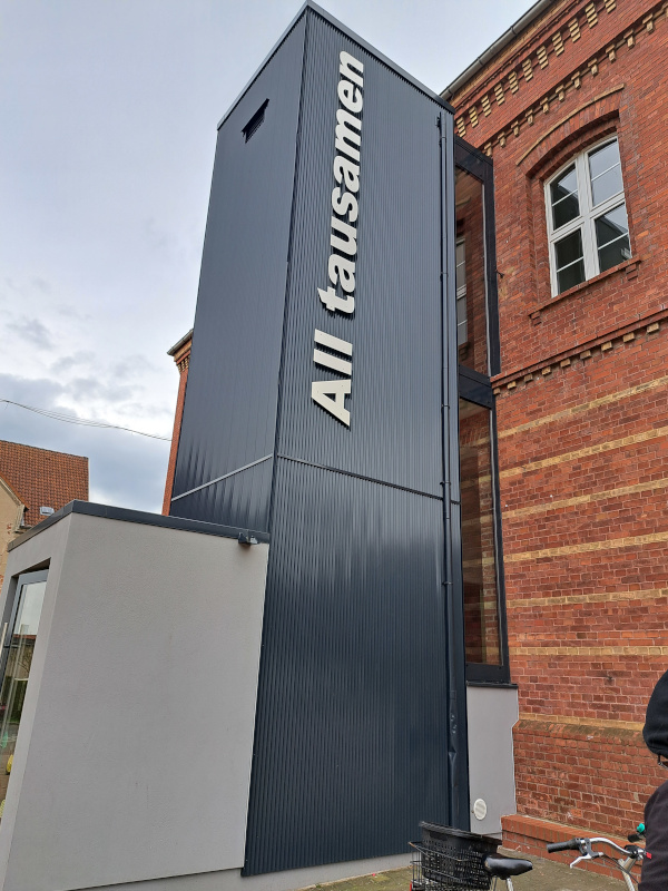 Foto des Fahrstuhls der Stadtbibliothek Altentreptow mit der (plattdeutschen) Aufschrift "All tausamen".